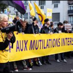 en manifestation : au premier plan une personne tient un megaphone, devant une bannière annonçant "stop aux mutilations intersexes"